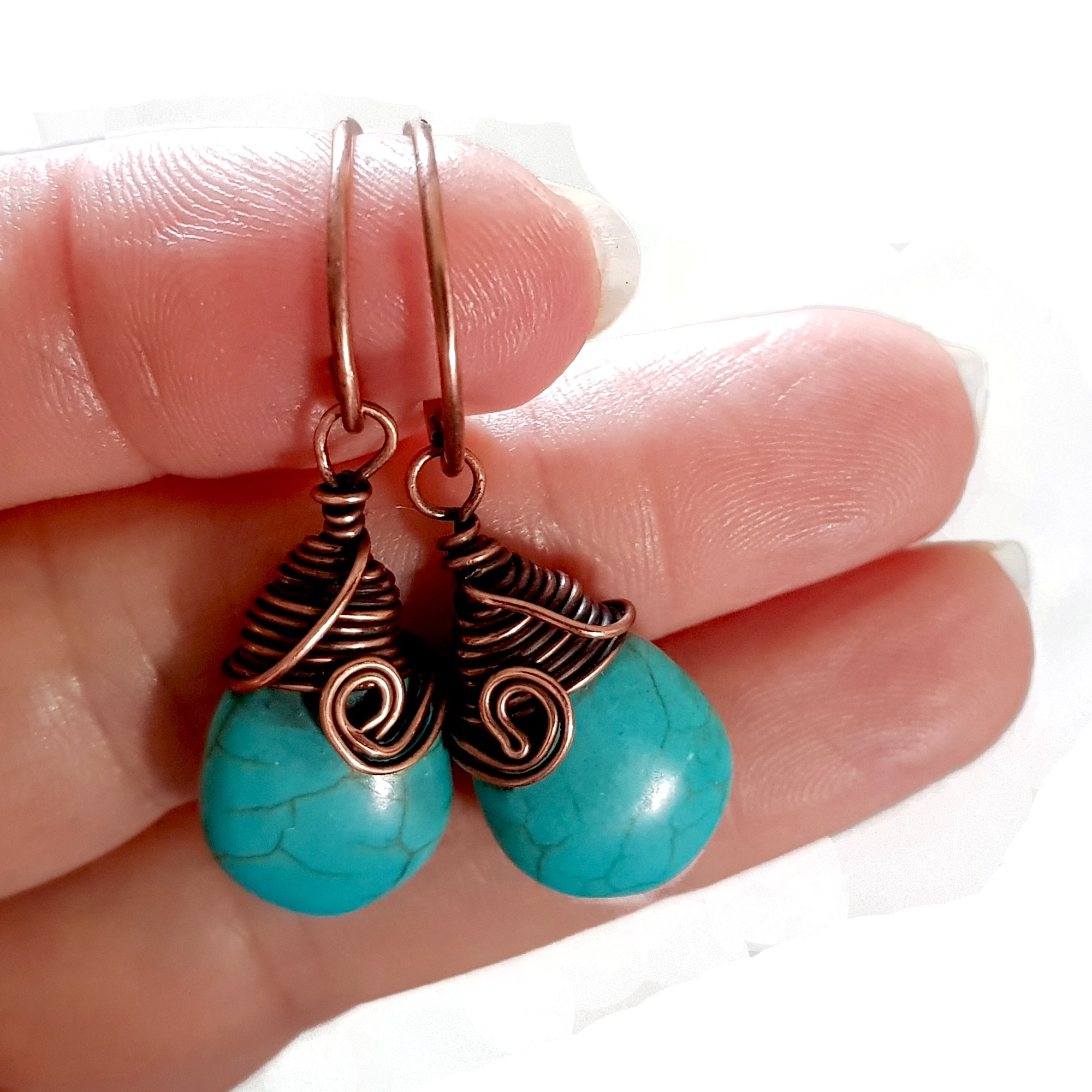 Turquoise blue howlite earrings with copper wire wrapping and handmade circle ear wires, elegantly displayed in a velvet pouch.