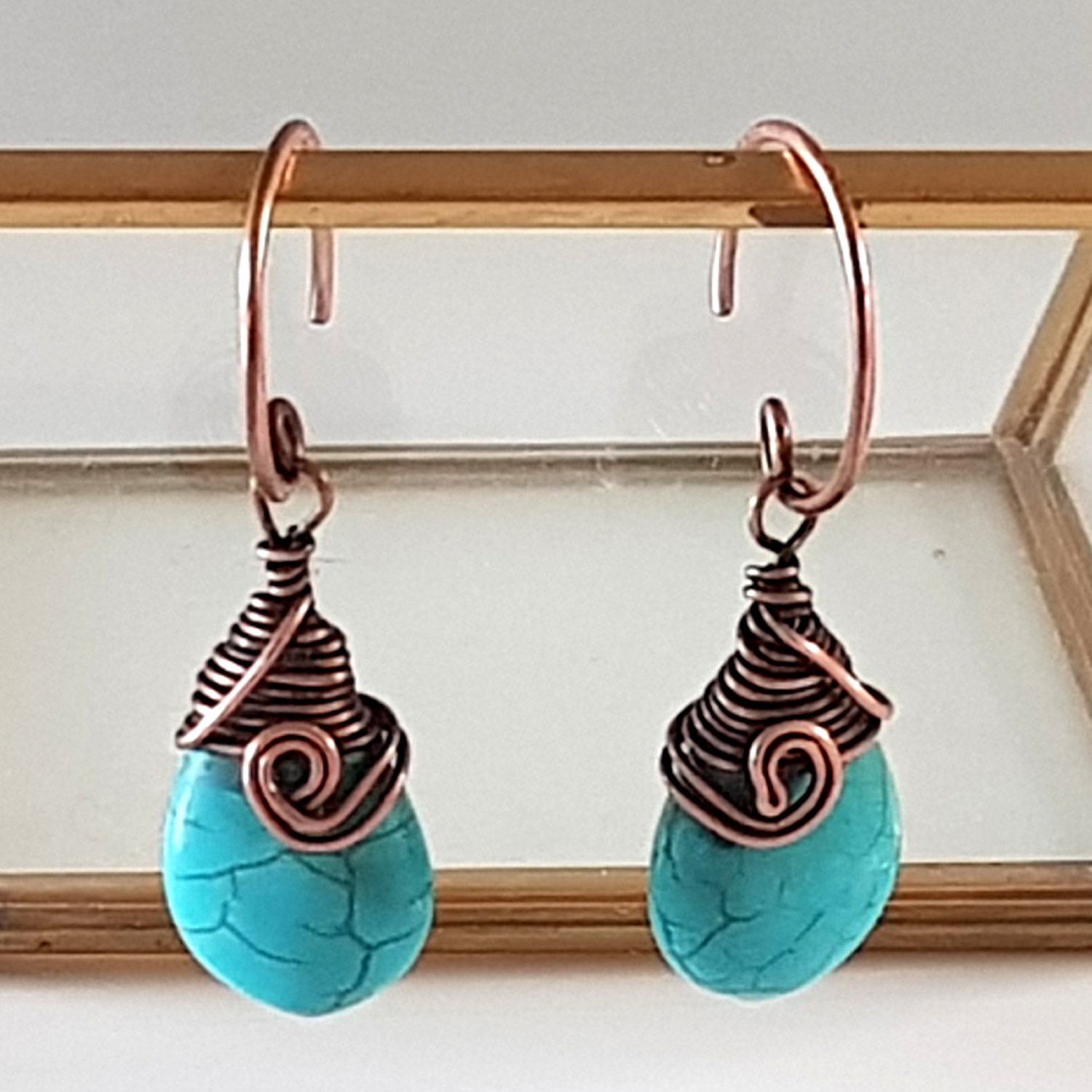 Turquoise blue howlite earrings with copper wire wrapping and handmade circle ear wires, elegantly displayed in a velvet pouch.