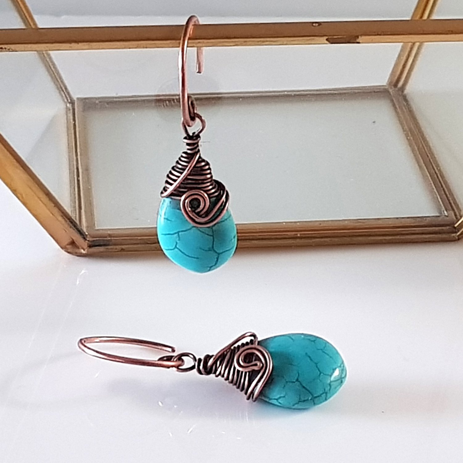 Turquoise blue howlite earrings with copper wire wrapping and handmade circle ear wires, elegantly displayed in a velvet pouch.