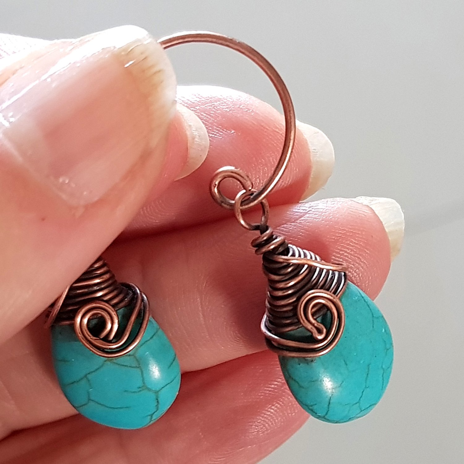 Turquoise blue howlite earrings with copper wire wrapping and handmade circle ear wires, elegantly displayed in a velvet pouch.