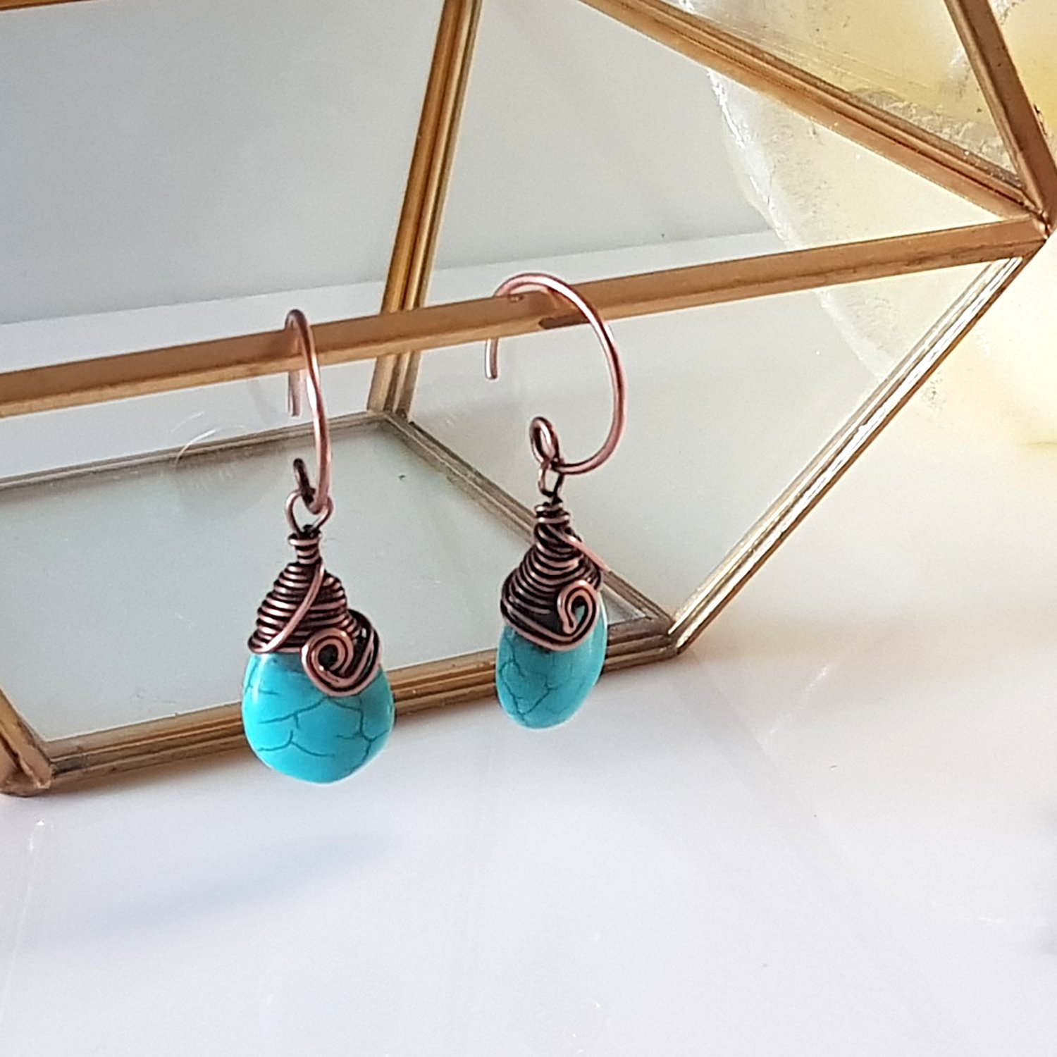 Turquoise blue howlite earrings with copper wire wrapping and handmade circle ear wires, elegantly displayed in a velvet pouch.