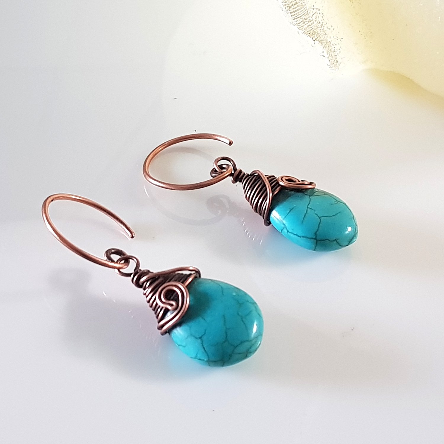 Turquoise blue howlite earrings with copper wire wrapping and handmade circle ear wires, elegantly displayed in a velvet pouch.