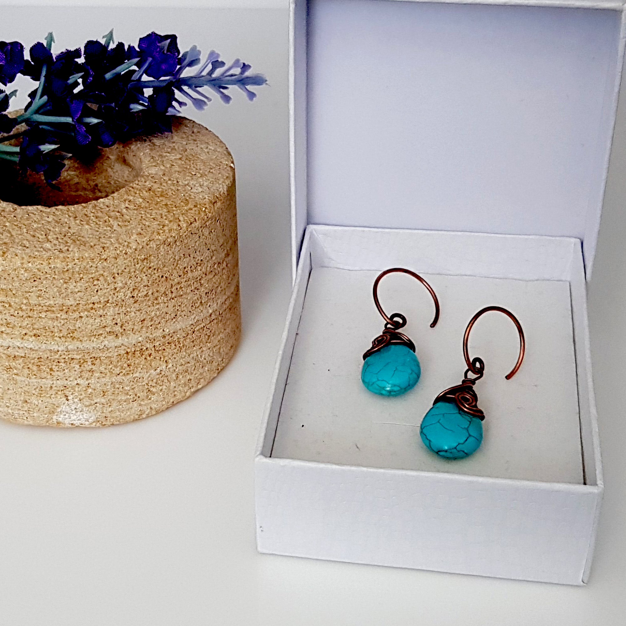 Turquoise blue howlite earrings with copper wire wrapping and handmade circle ear wires, elegantly displayed in a velvet pouch.