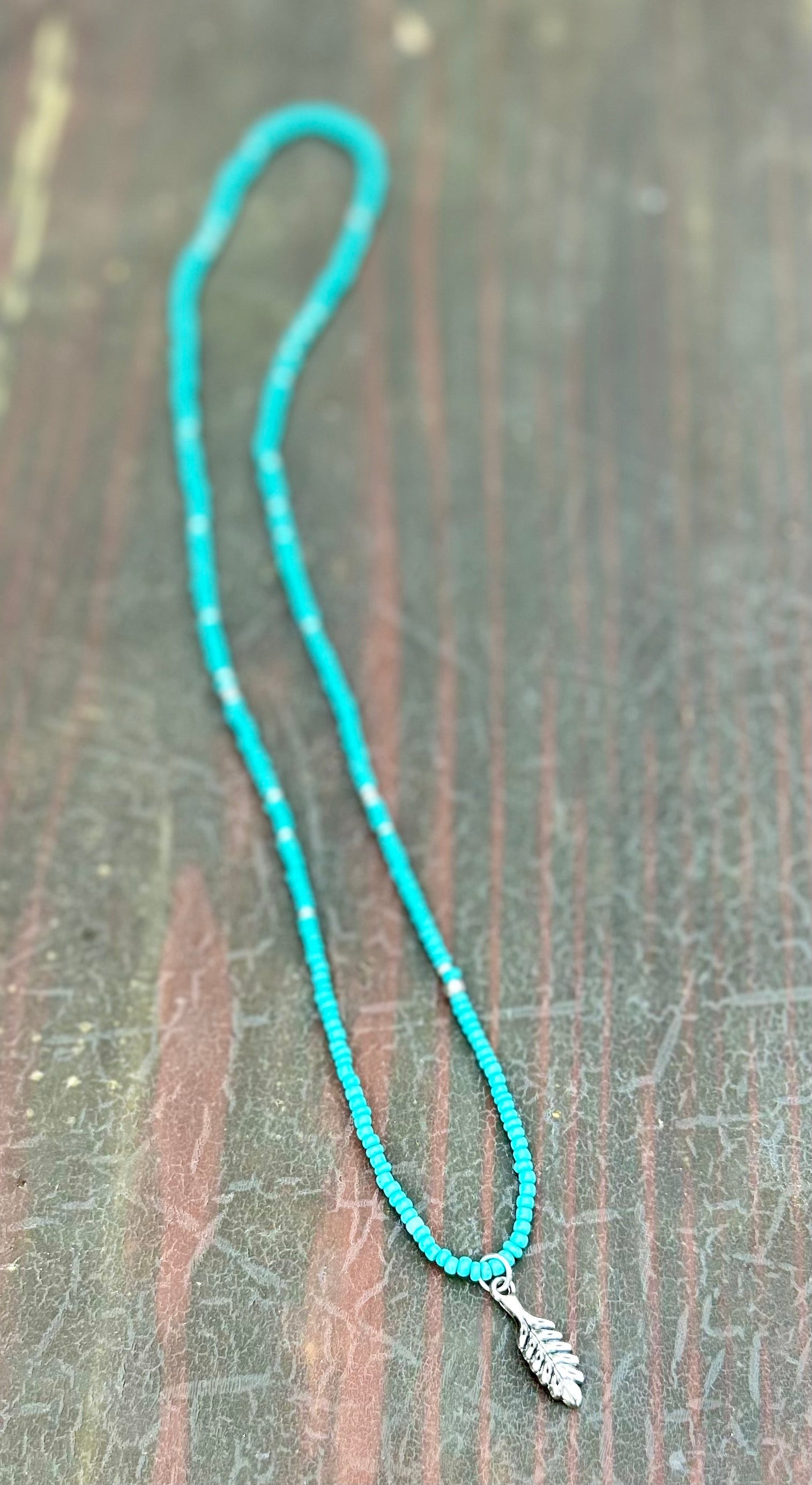 Turquoise Boho Seed Bead Necklace featuring silver beads and a silver feather charm, showcasing a vibrant and stylish design.