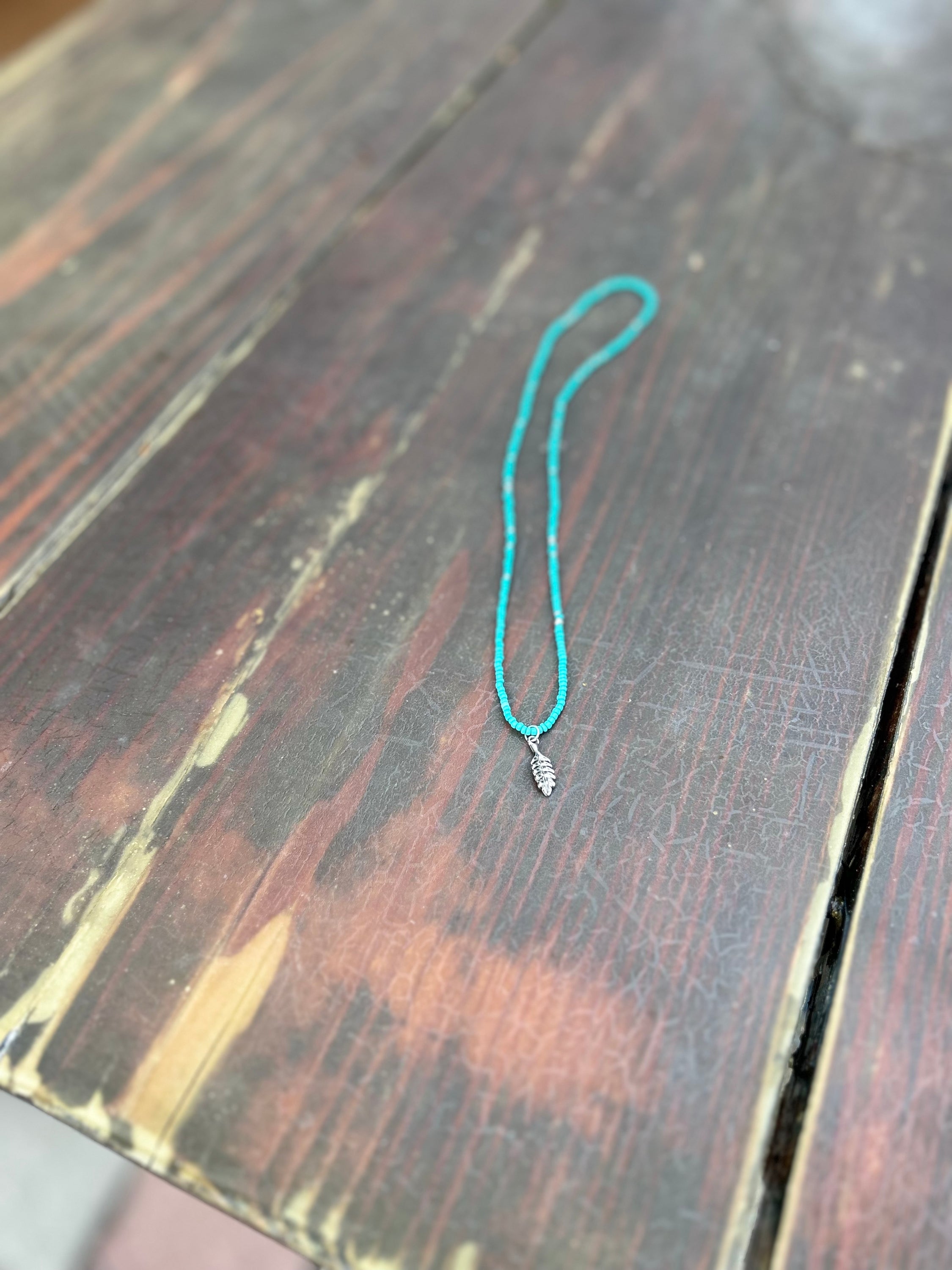 Turquoise Boho Seed Bead Necklace featuring silver beads and a silver feather charm, showcasing a vibrant and stylish design.