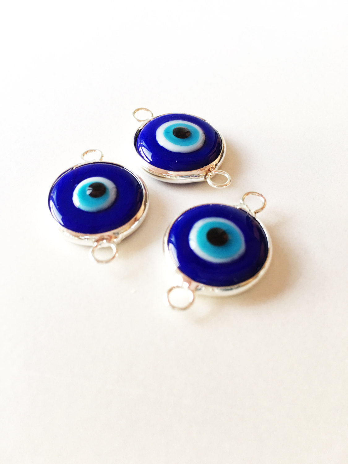 Two connectors glass evil eye charms in blue, yellow, and turquoise colors, featuring silver plating, ideal for jewelry making.