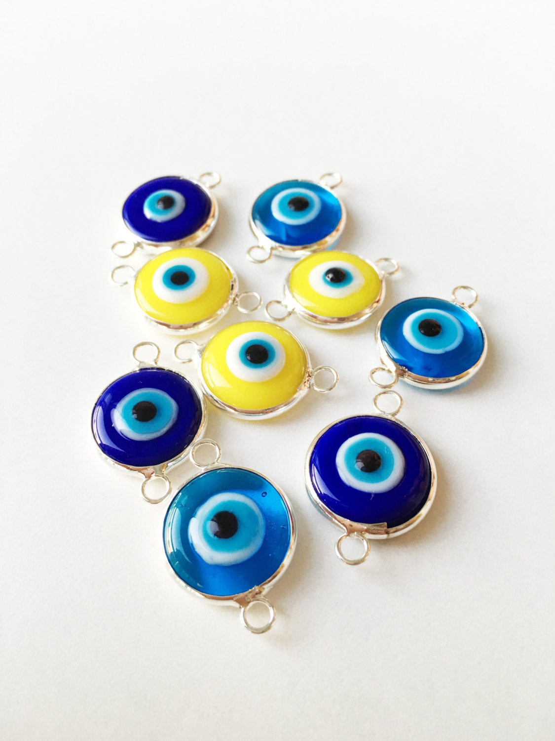 Two connectors glass evil eye charms in blue, yellow, and turquoise colors, featuring silver plating, ideal for jewelry making.