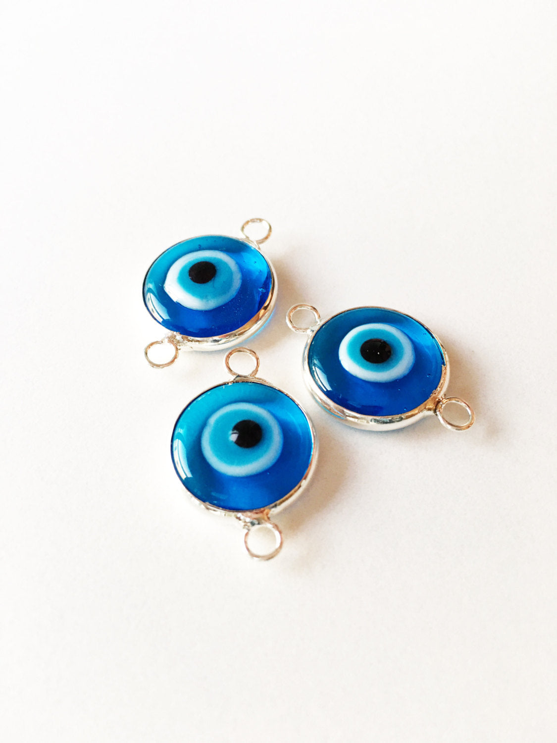 Two connectors glass evil eye charms in blue, yellow, and turquoise colors, featuring silver plating, ideal for jewelry making.