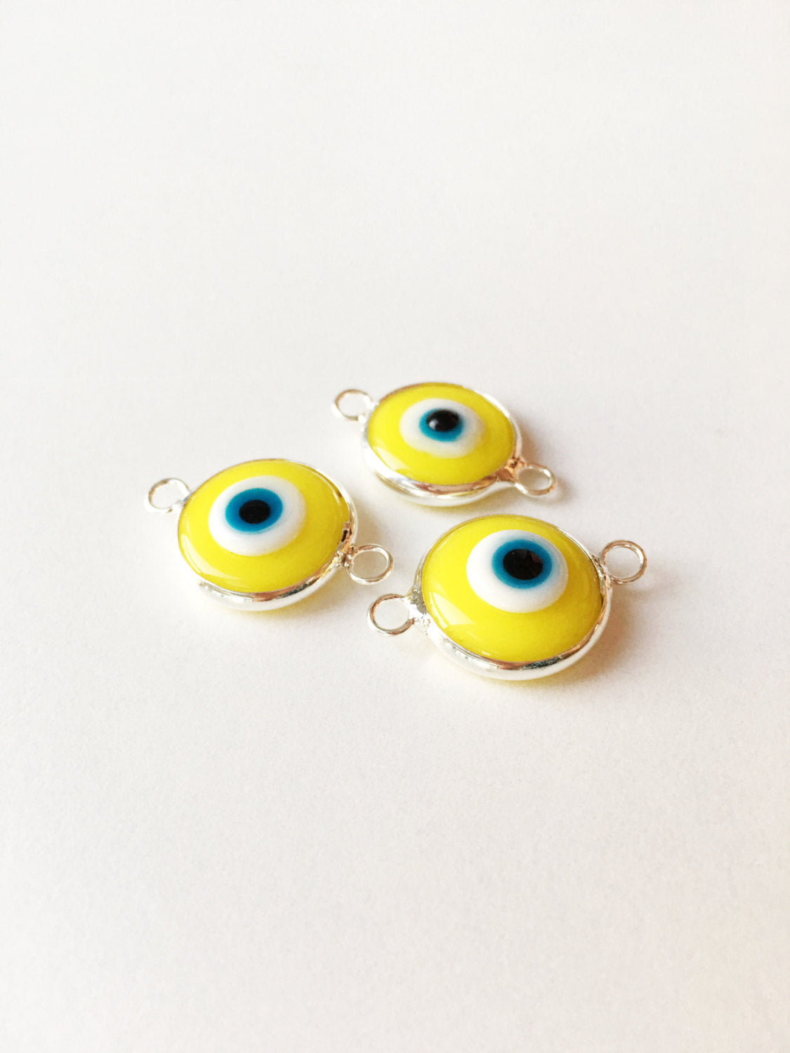 Two connectors glass evil eye charms in blue, yellow, and turquoise colors, featuring silver plating, ideal for jewelry making.