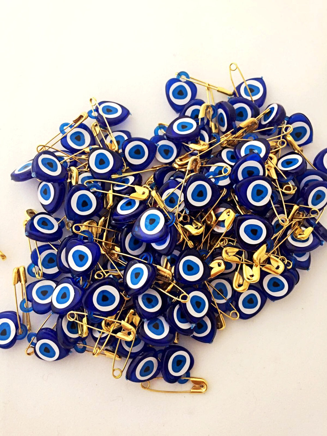 A collection of 100 tiny heart-shaped resin safety pins featuring evil eye beads in vibrant colors, perfect for wedding favors.