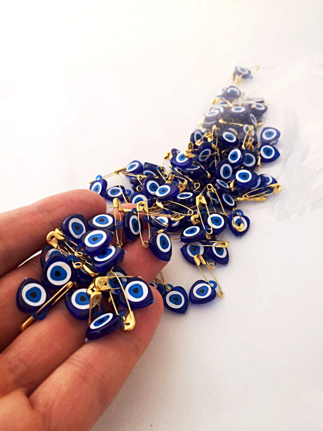 A collection of 100 tiny heart-shaped resin safety pins featuring evil eye beads in vibrant colors, perfect for wedding favors.