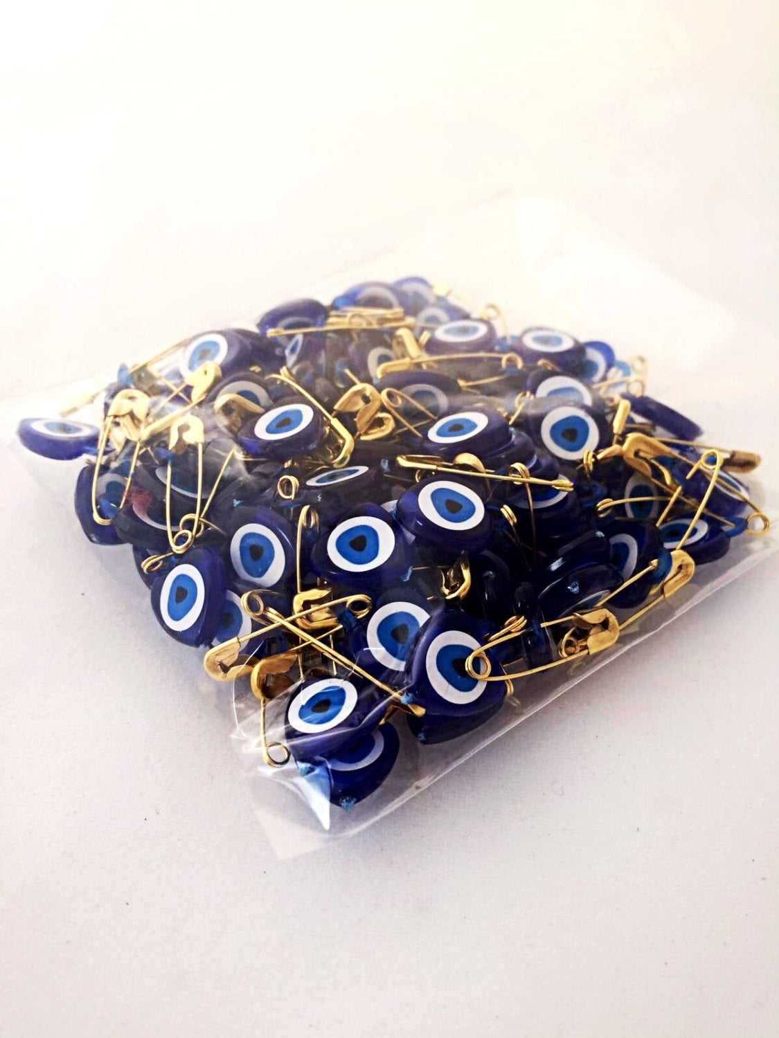 A collection of 100 tiny heart-shaped resin safety pins featuring evil eye beads in vibrant colors, perfect for wedding favors.