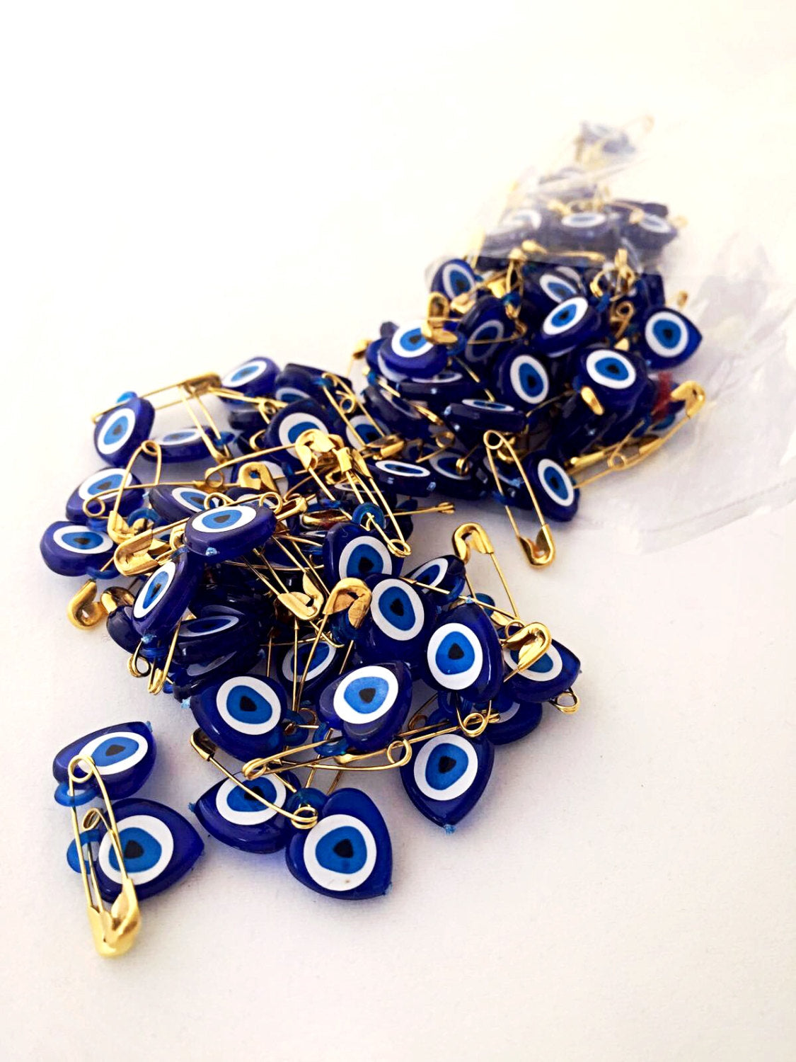 A collection of 100 tiny heart-shaped resin safety pins featuring evil eye beads in vibrant colors, perfect for wedding favors.