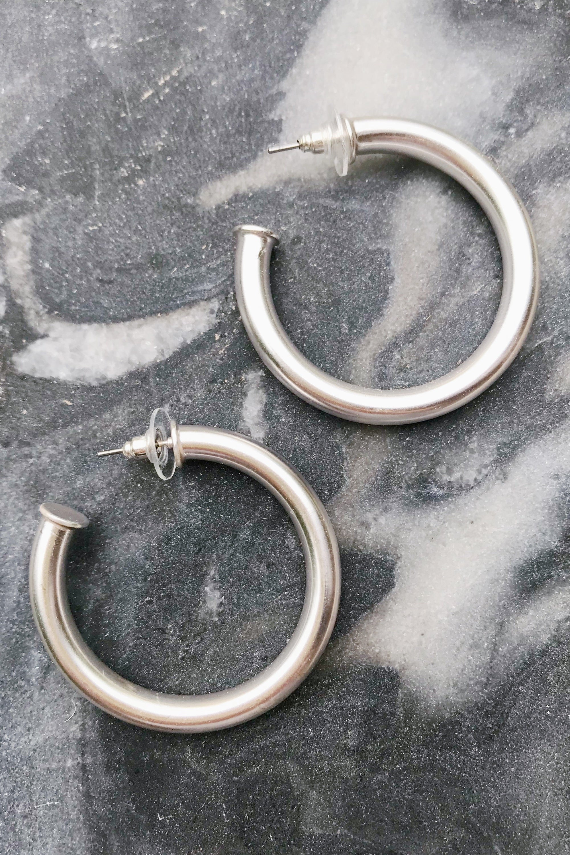 Small silver hoop earrings with a lightweight tube style and matte finish, measuring 1.5 inches in diameter.