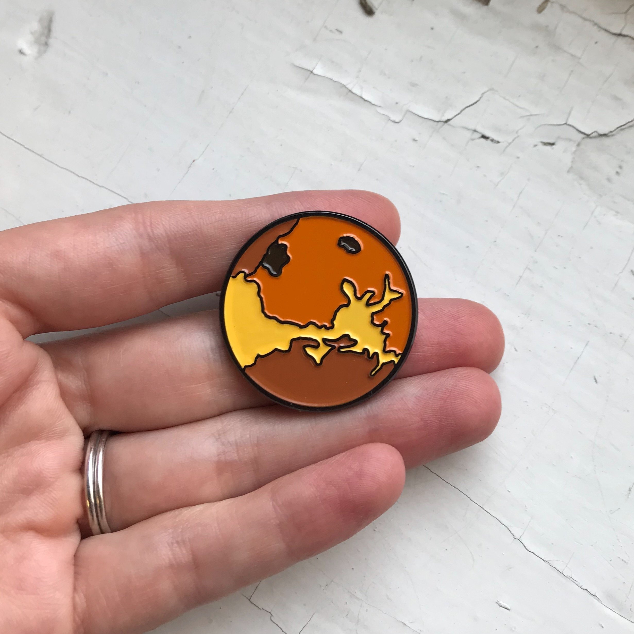 Venus Enamel Pin featuring a colorful illustration of the planet Venus, designed by Lauren Beacham, perfect for jackets and backpacks.