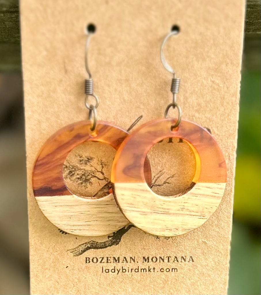 A pair of lightweight hoop earrings made from walnut wood and amber-colored resin, showcasing unique wood grain patterns.