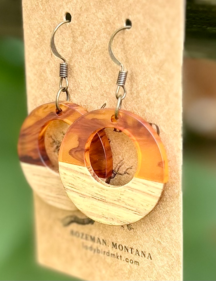 A pair of lightweight hoop earrings made from walnut wood and amber-colored resin, showcasing unique wood grain patterns.