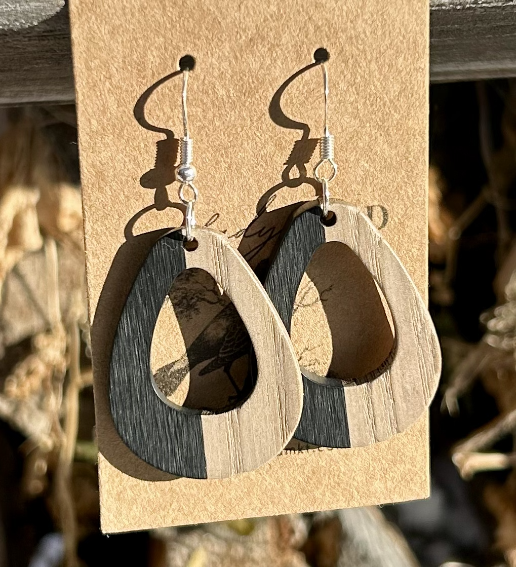 A pair of oval hoop earrings made from walnut wood and black resin, showcasing unique wood grain patterns and a modern design.