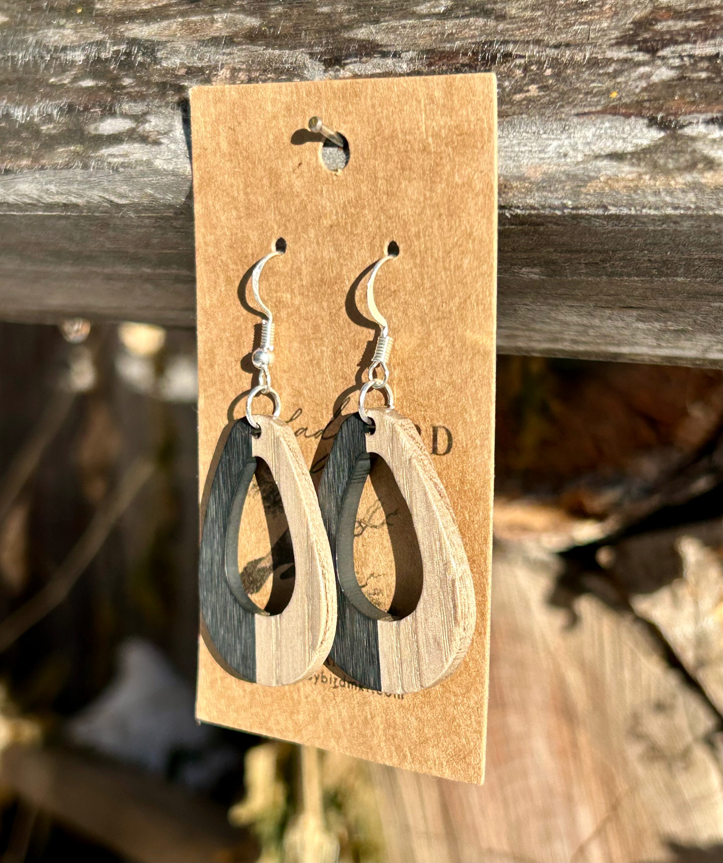 A pair of oval hoop earrings made from walnut wood and black resin, showcasing unique wood grain patterns and a modern design.