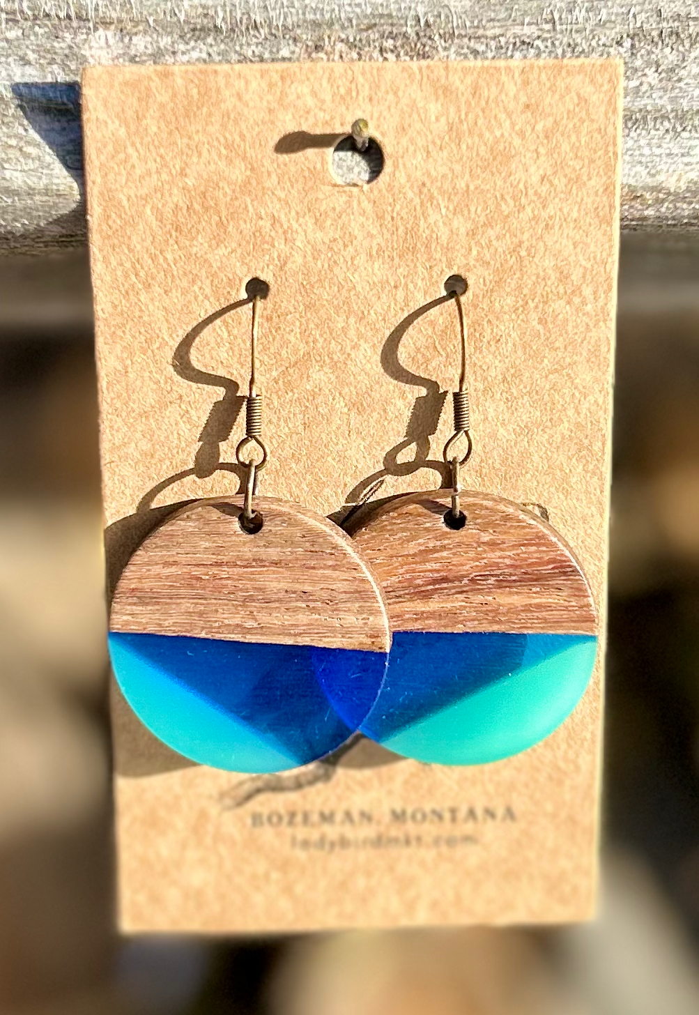 A pair of circle earrings made from walnut wood and blue resin, showcasing a geometric pattern and natural wood grain.