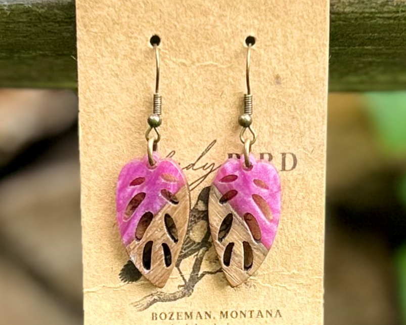 A pair of leaf-shaped earrings made from walnut wood and magenta resin, showcasing unique wood grain patterns and vibrant color.