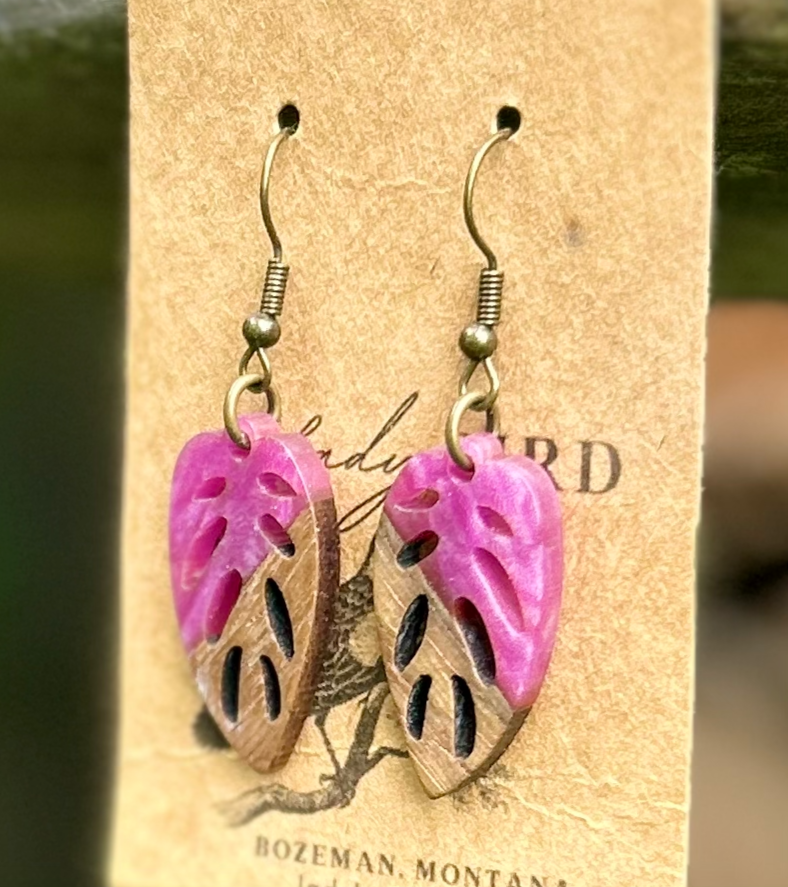 A pair of leaf-shaped earrings made from walnut wood and magenta resin, showcasing unique wood grain patterns and vibrant color.