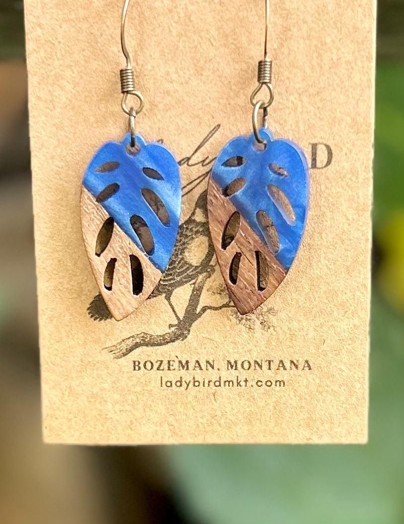 A pair of leaf-shaped earrings made from walnut wood and royal blue resin, showcasing their unique natural grain and vibrant color.