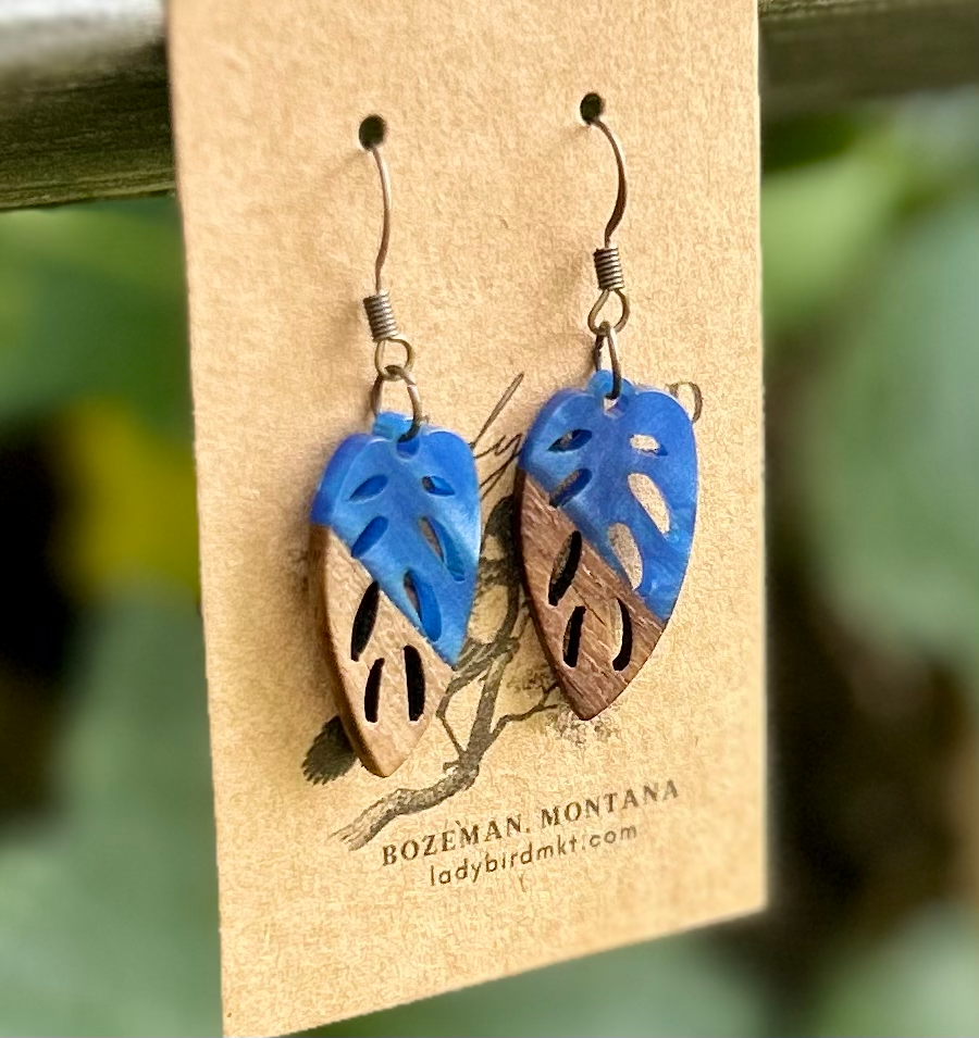 A pair of leaf-shaped earrings made from walnut wood and royal blue resin, showcasing their unique natural grain and vibrant color.