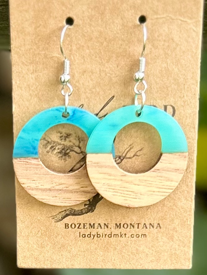 A pair of lightweight hoop earrings made from walnut wood and pearly opaque turquoise resin, showcasing unique wood grain patterns.