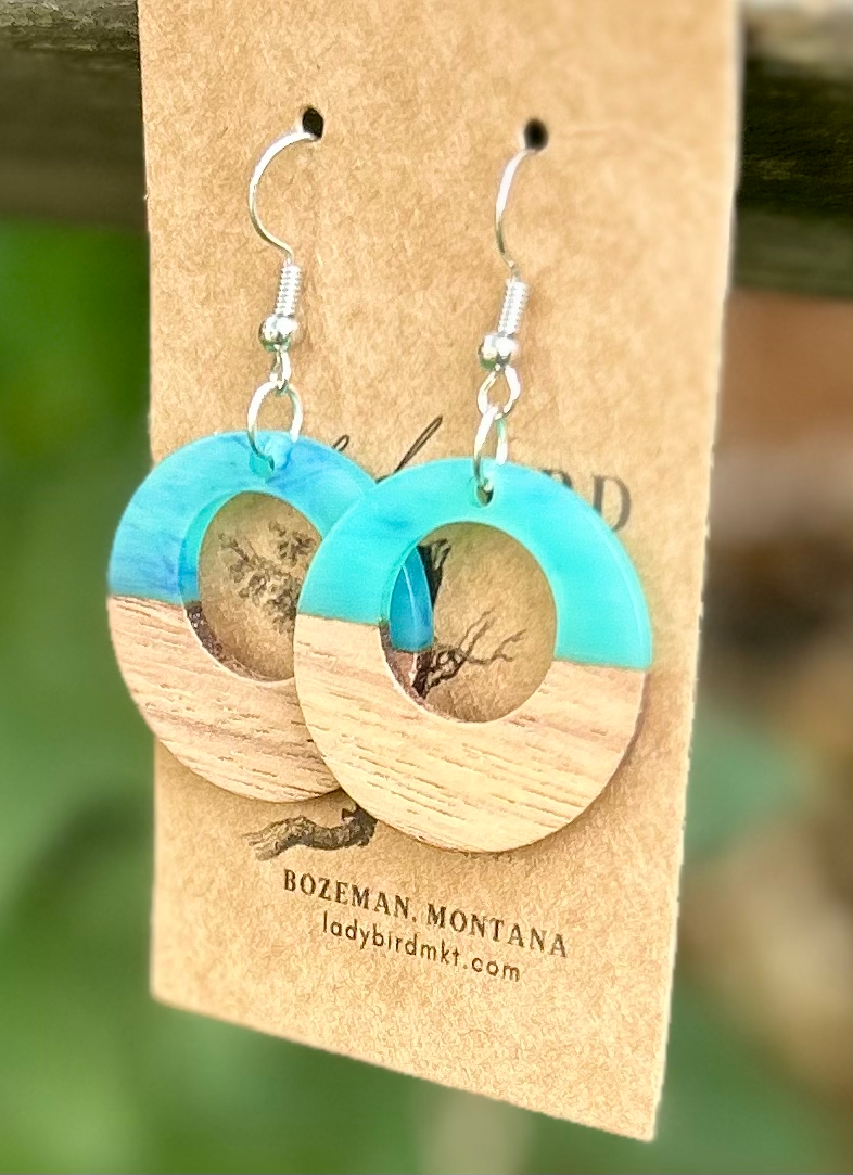 A pair of lightweight hoop earrings made from walnut wood and pearly opaque turquoise resin, showcasing unique wood grain patterns.