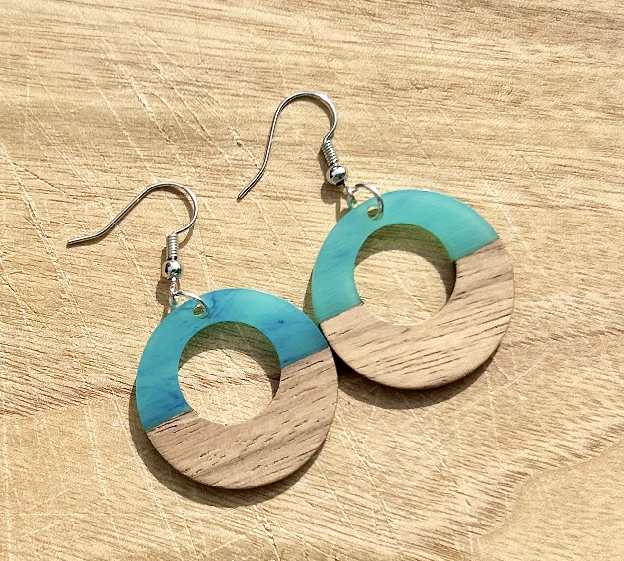 A pair of lightweight hoop earrings made from walnut wood and pearly opaque turquoise resin, showcasing unique wood grain patterns.