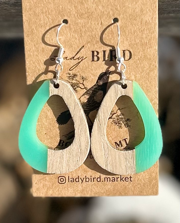 A pair of oval earrings made from walnut wood and turquoise resin, showcasing unique wood grain patterns and vibrant color.