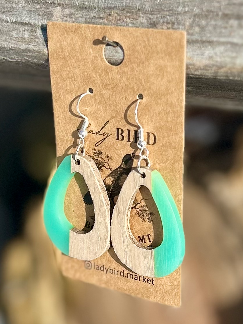 A pair of oval earrings made from walnut wood and turquoise resin, showcasing unique wood grain patterns and vibrant color.