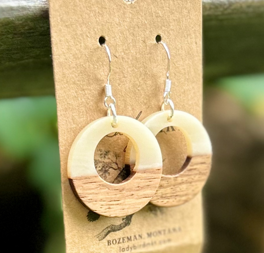 A pair of lightweight hoop earrings made from walnut wood and pearly white resin, showcasing unique wood grain patterns.