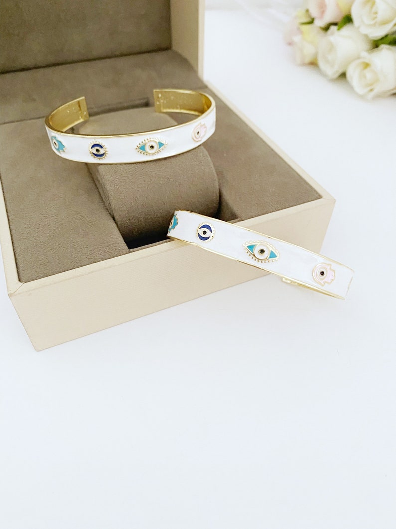 Elegant white cuff bracelet featuring a movable evil eye hamsa hand charm, crafted from tarnish-resistant stainless steel.