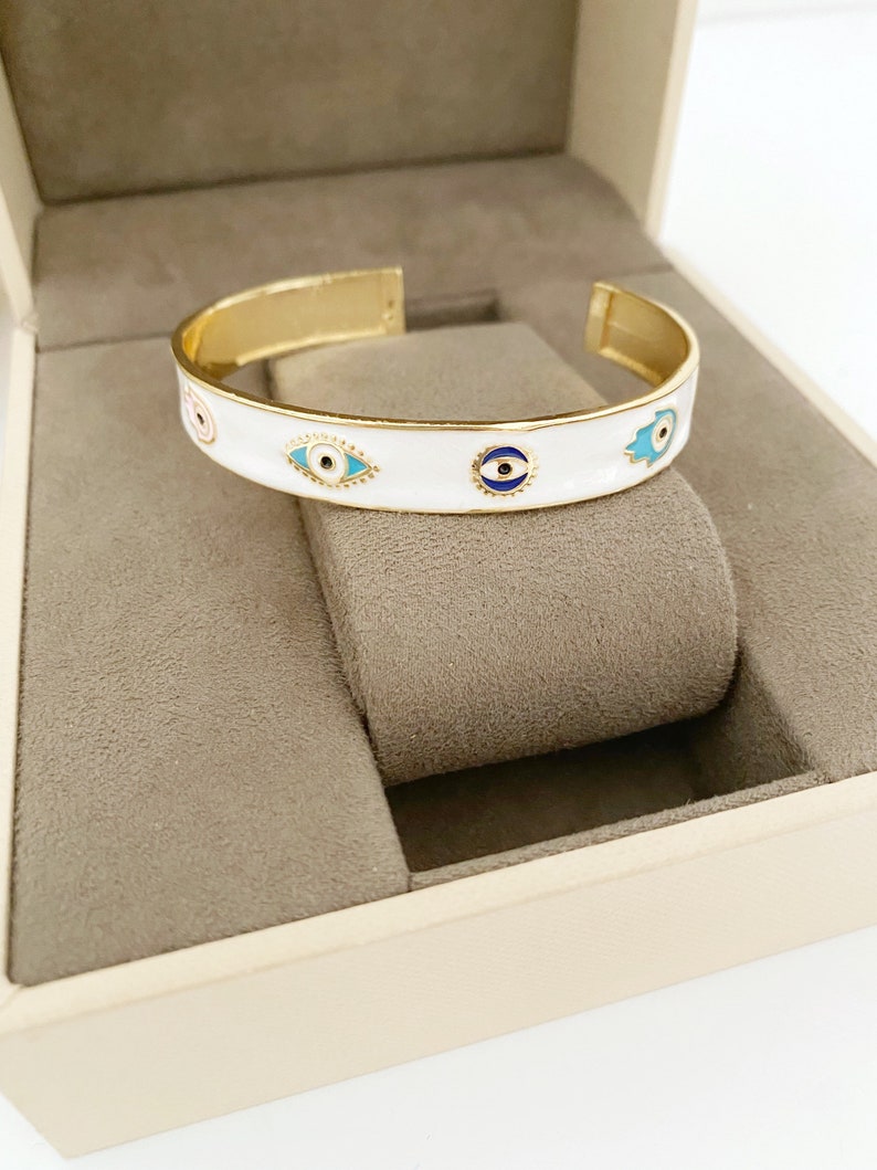 Elegant white cuff bracelet featuring a movable evil eye hamsa hand charm, crafted from tarnish-resistant stainless steel.