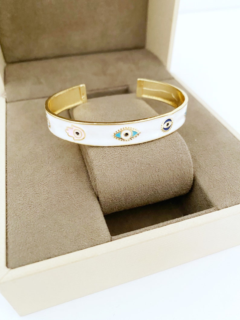 Elegant white cuff bracelet featuring a movable evil eye hamsa hand charm, crafted from tarnish-resistant stainless steel.