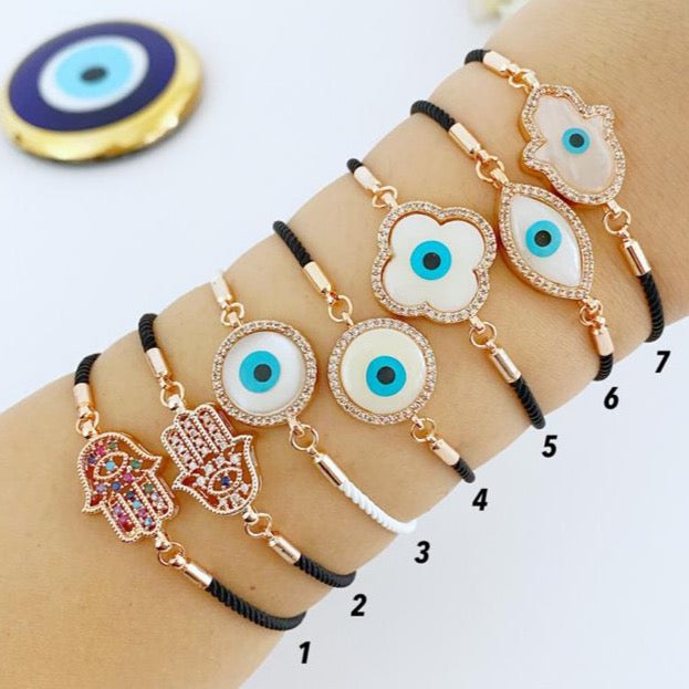 A stylish White Evil Eye Bracelet featuring a Hamsa charm on a black string, adorned with zirconia around a clover charm.