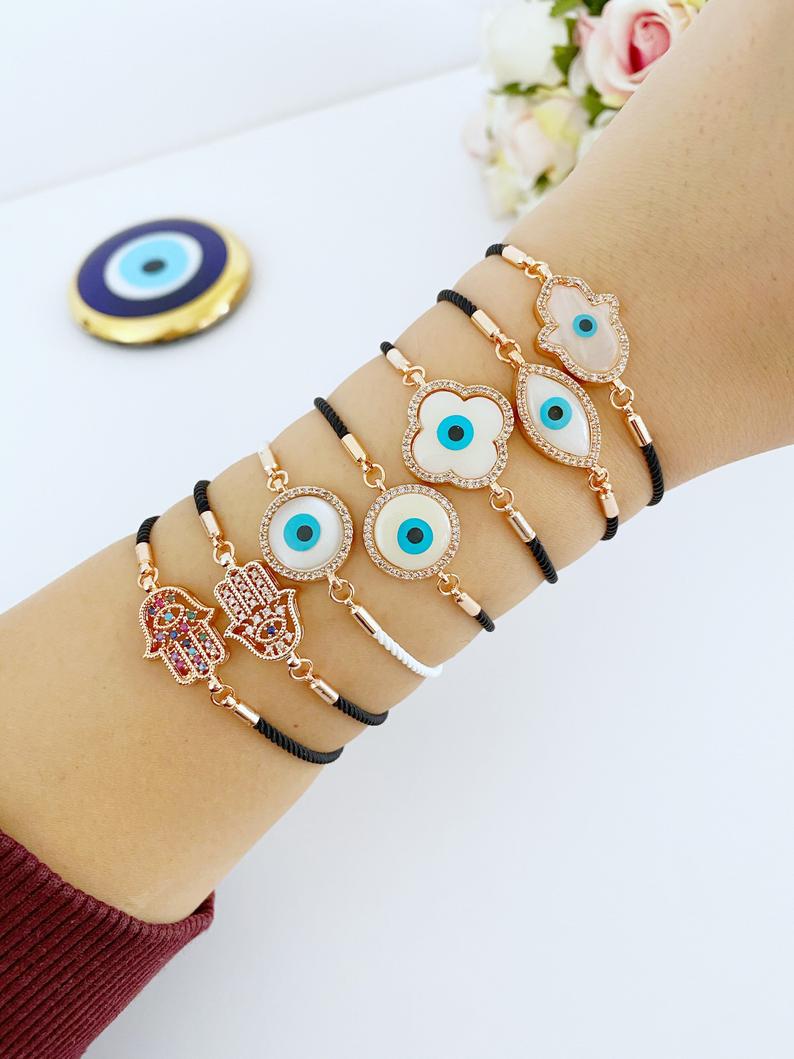 A stylish White Evil Eye Bracelet featuring a Hamsa charm on a black string, adorned with zirconia around a clover charm.