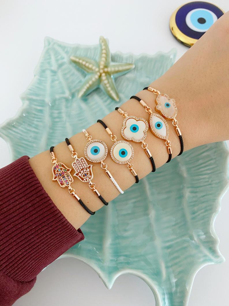 A stylish White Evil Eye Bracelet featuring a Hamsa charm on a black string, adorned with zirconia around a clover charm.