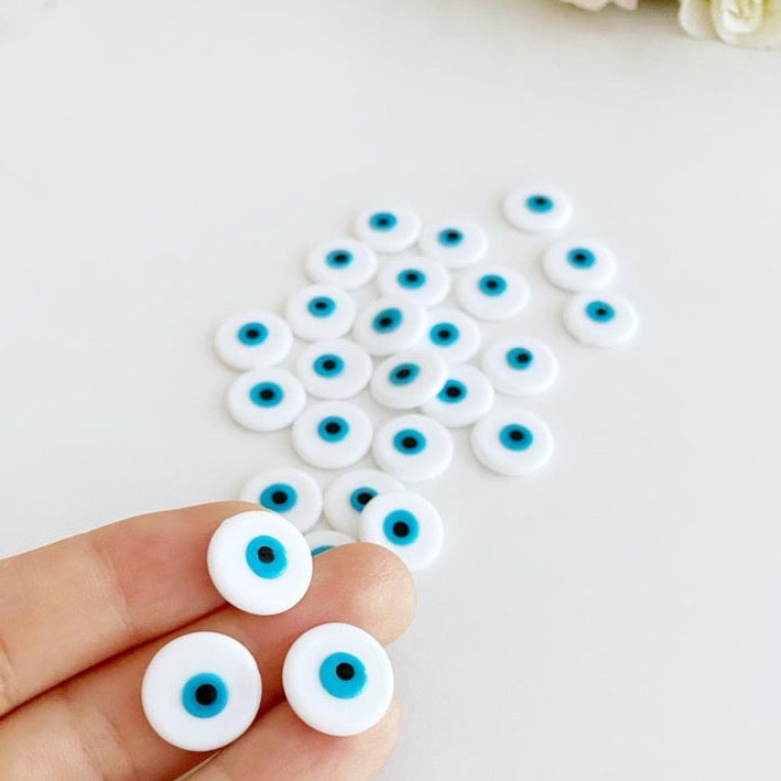 A collection of white evil eye cabochons made from Murano glass, showcasing their round shape and unique design.