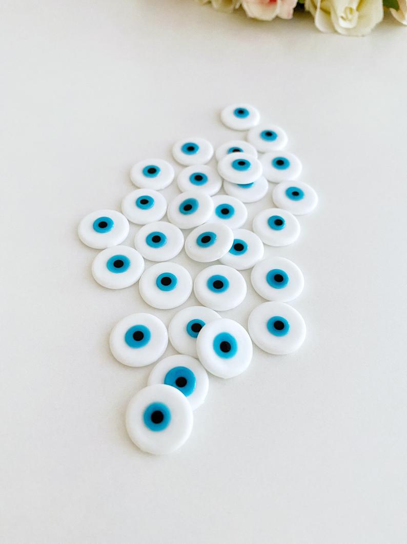 A collection of white evil eye cabochons made from Murano glass, showcasing their round shape and unique design.