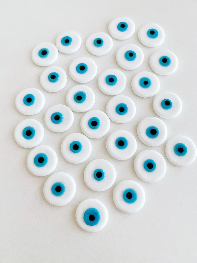 A collection of white evil eye cabochons made from Murano glass, showcasing their round shape and unique design.