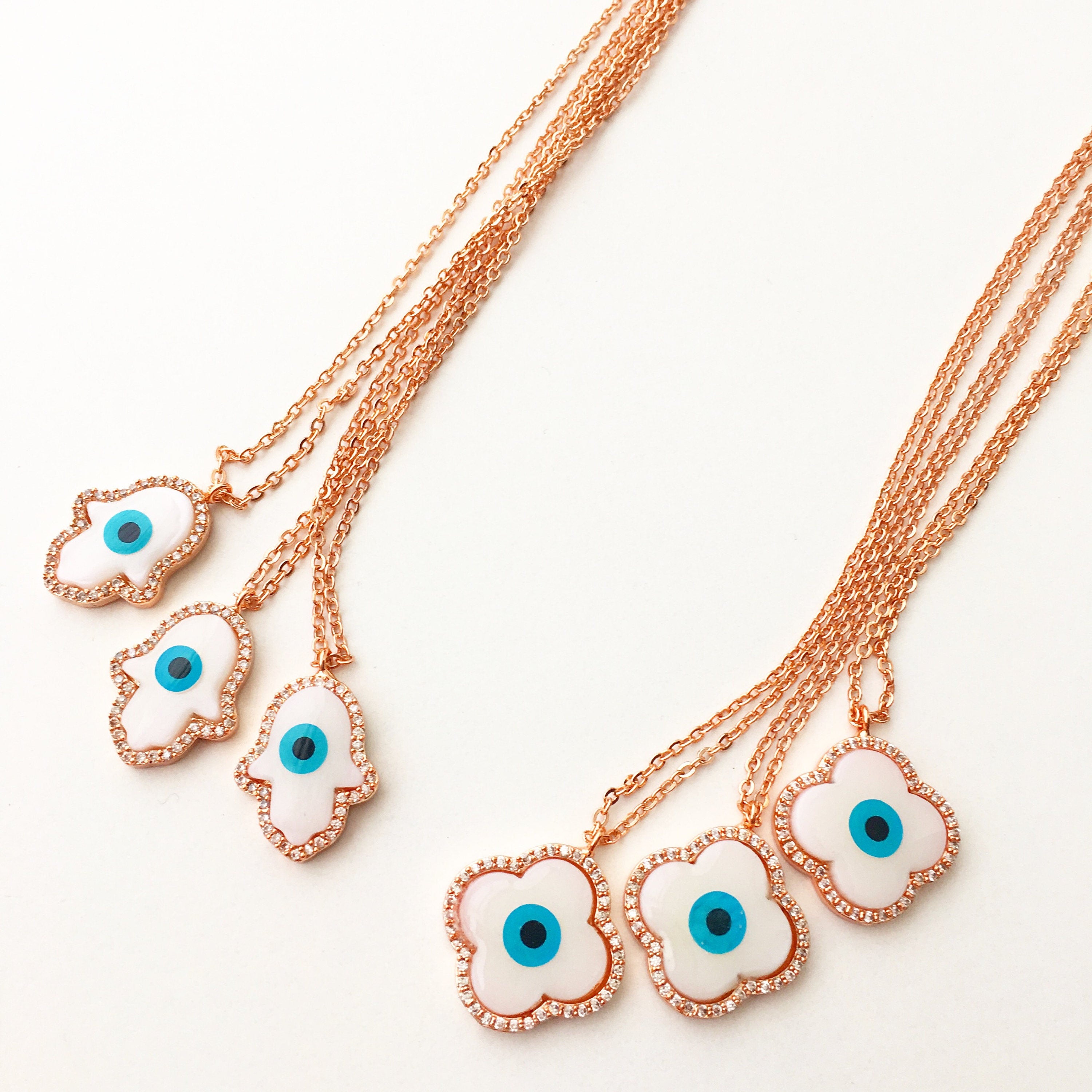 A beautiful White Evil Eye Necklace featuring a Hamsa Hand and Clover Charm, showcasing intricate details and a rose gold finish.