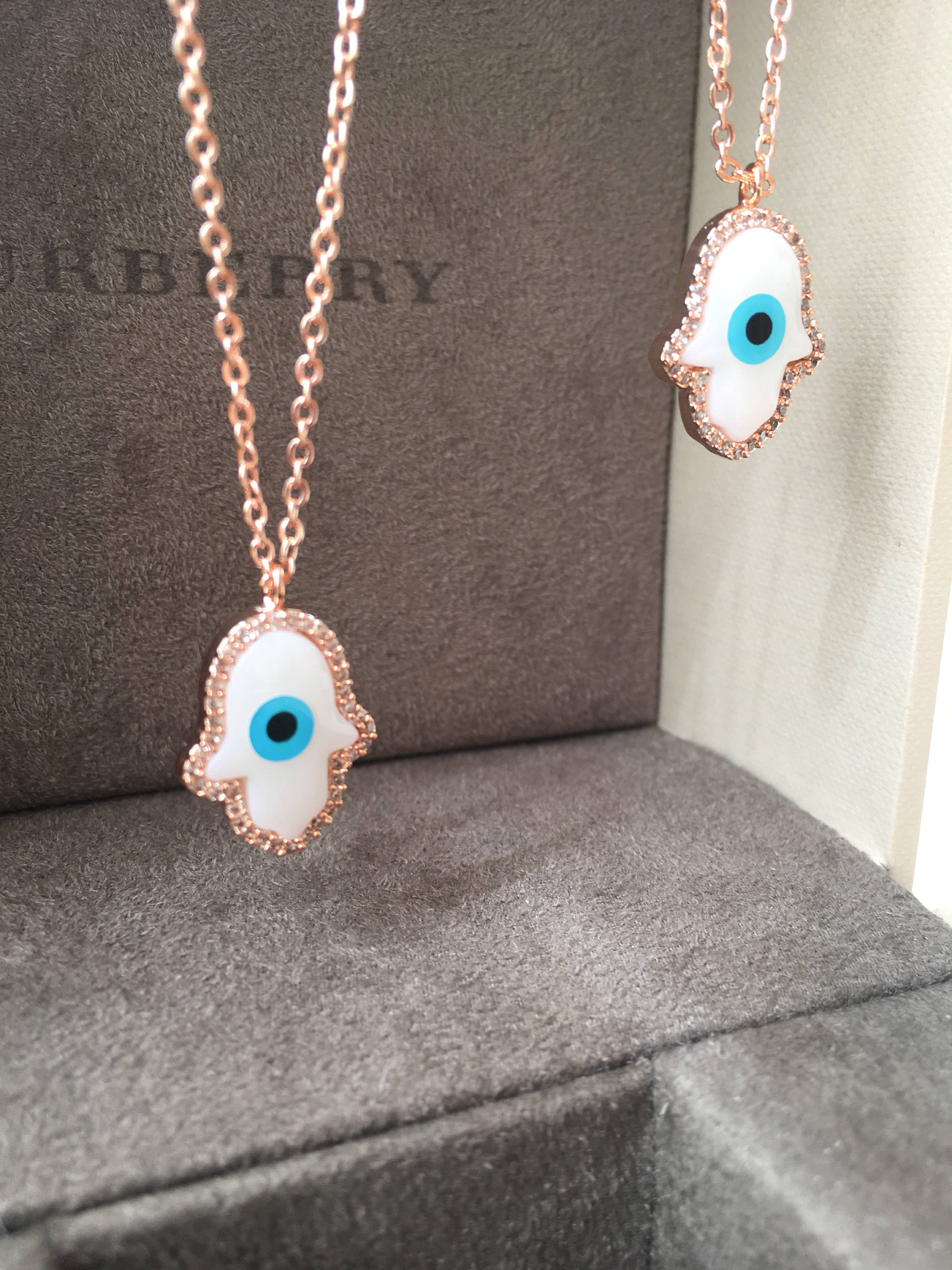 A beautiful White Evil Eye Necklace featuring a Hamsa Hand and Clover Charm, showcasing intricate details and a rose gold finish.