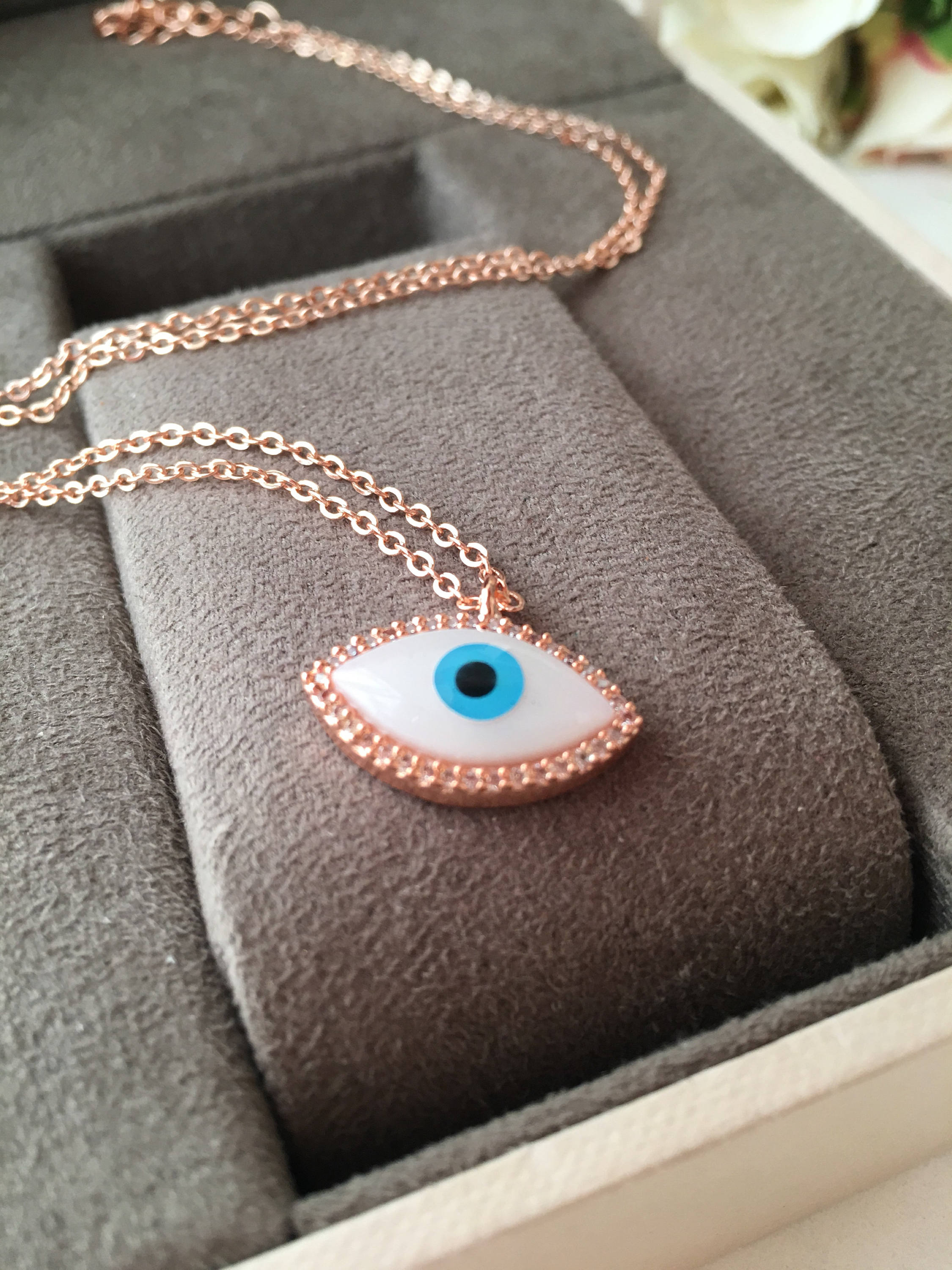 A beautiful White Evil Eye Necklace featuring a Hamsa Hand and Clover Charm, showcasing intricate details and a rose gold finish.