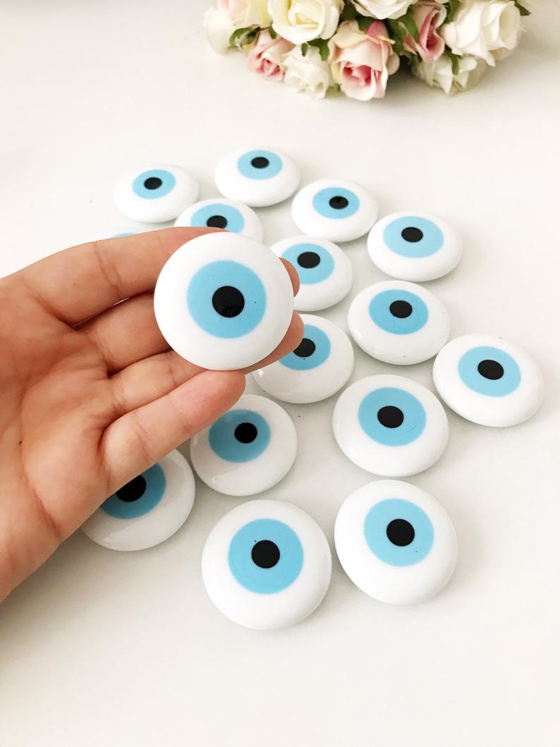 A white handmade evil eye glass bead magnet featuring a traditional Greek design, perfect for home decor and good luck.