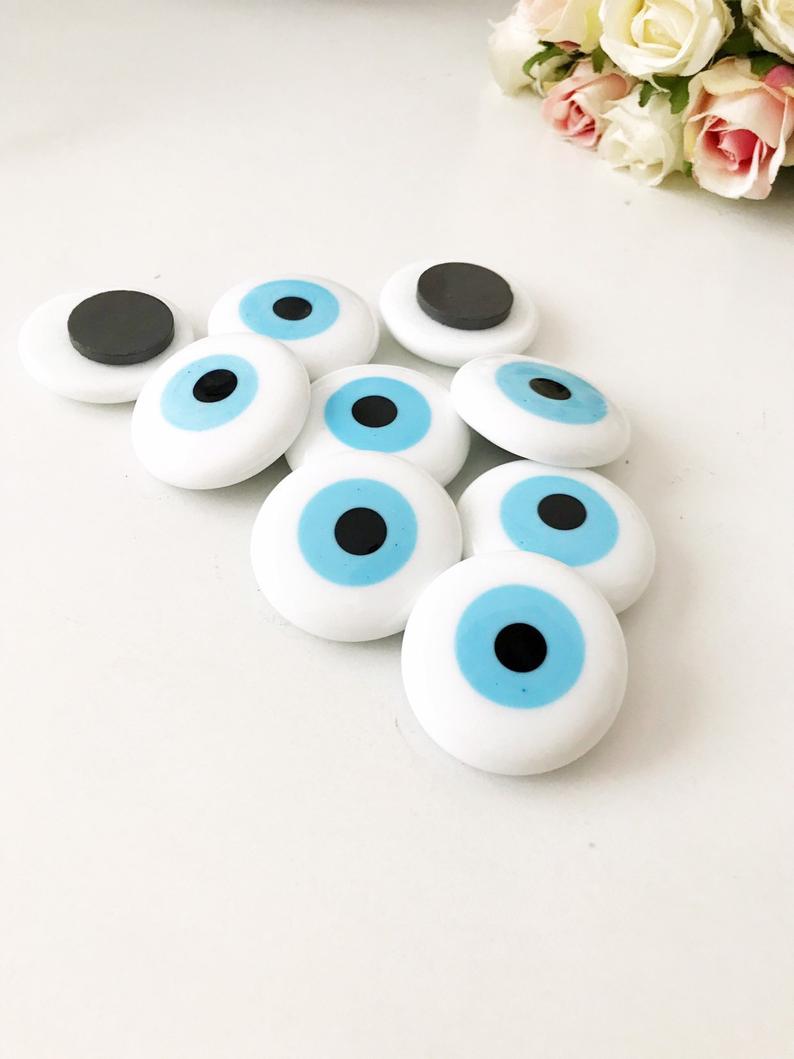 A white handmade evil eye glass bead magnet featuring a traditional Greek design, perfect for home decor and good luck.