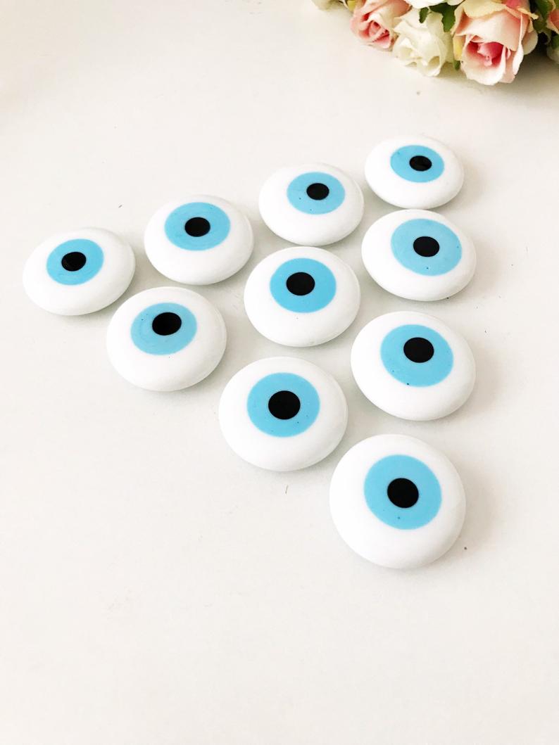 A white handmade evil eye glass bead magnet featuring a traditional Greek design, perfect for home decor and good luck.