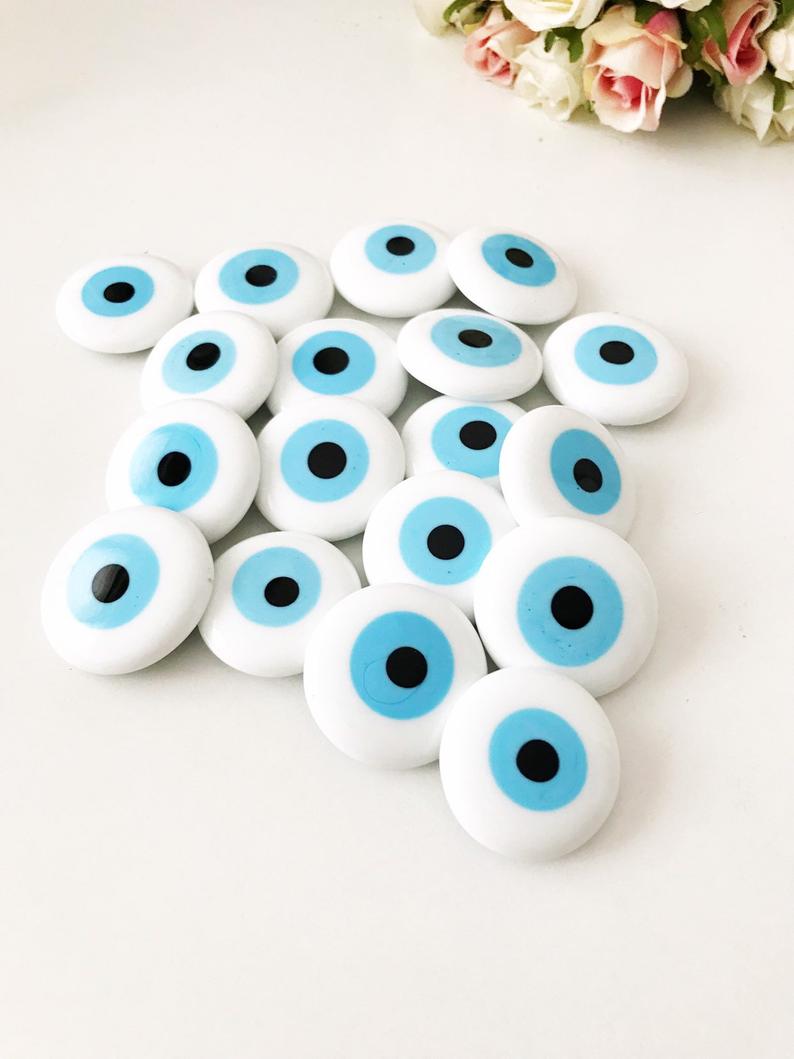 A white handmade evil eye glass bead magnet featuring a traditional Greek design, perfect for home decor and good luck.